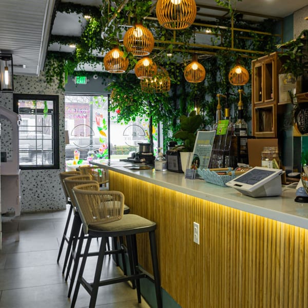 Interior of Good Life Clubhaus Juice Bar with a wooden counter, bar stools, and hanging plants.