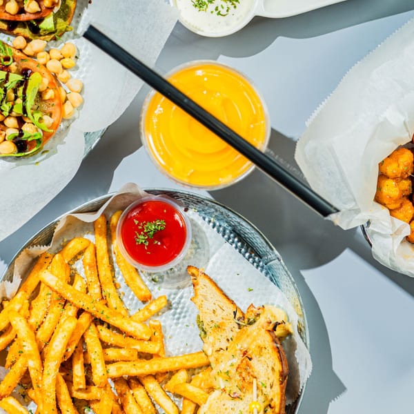 Overhead view of fries, a grilled cheese sandwich, a juice, and other snacks on a table.
