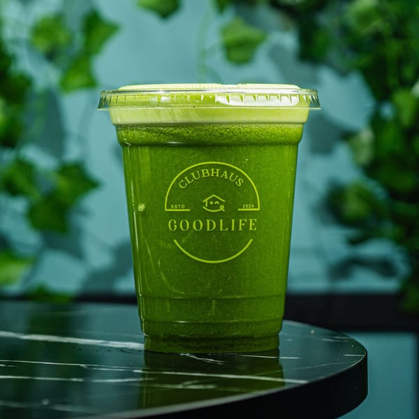 A Good Life Clubhaus green juice in a clear cup on a black marble table.